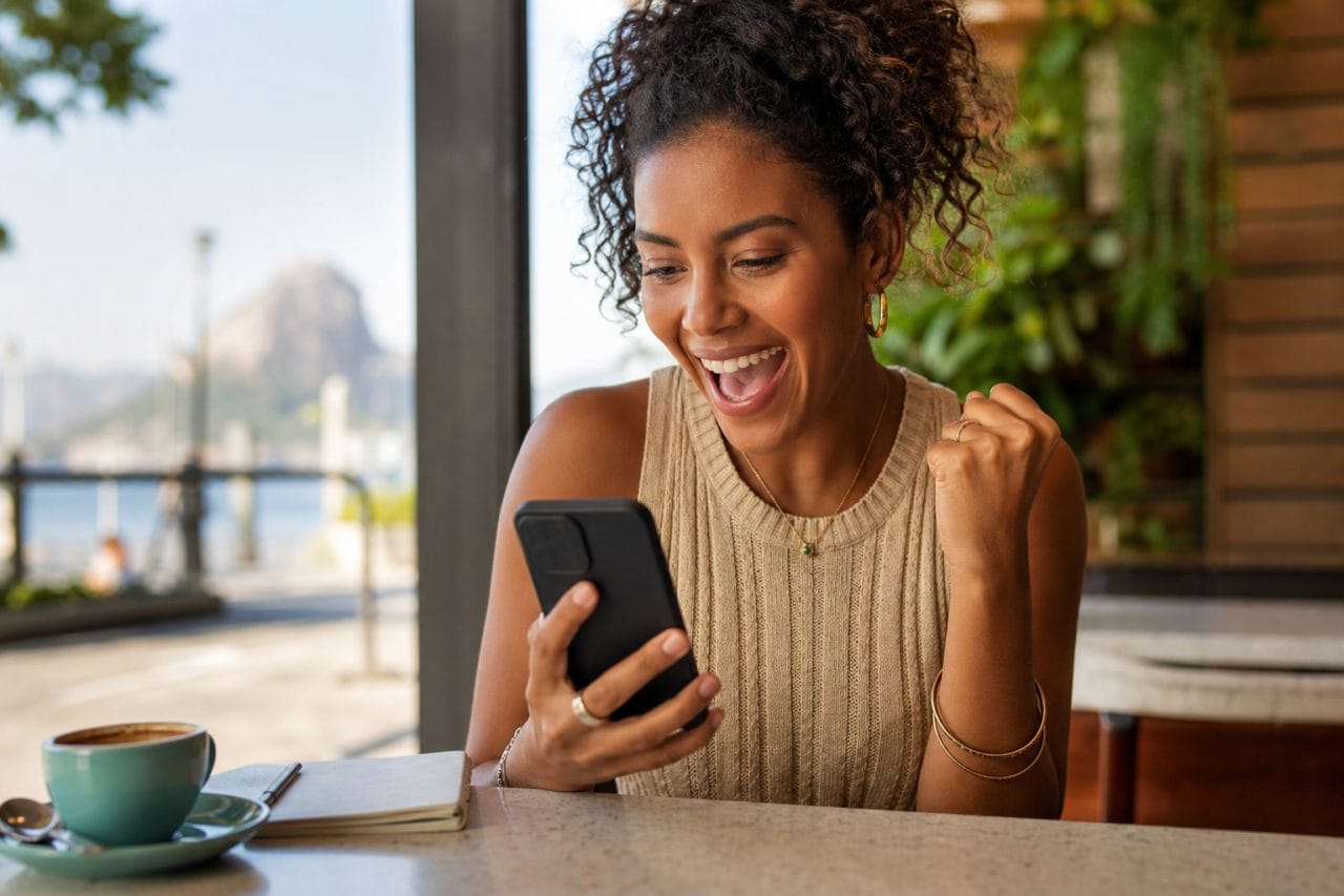 Mão segurando smartphone com notificação de milhas bônus em café elegante.